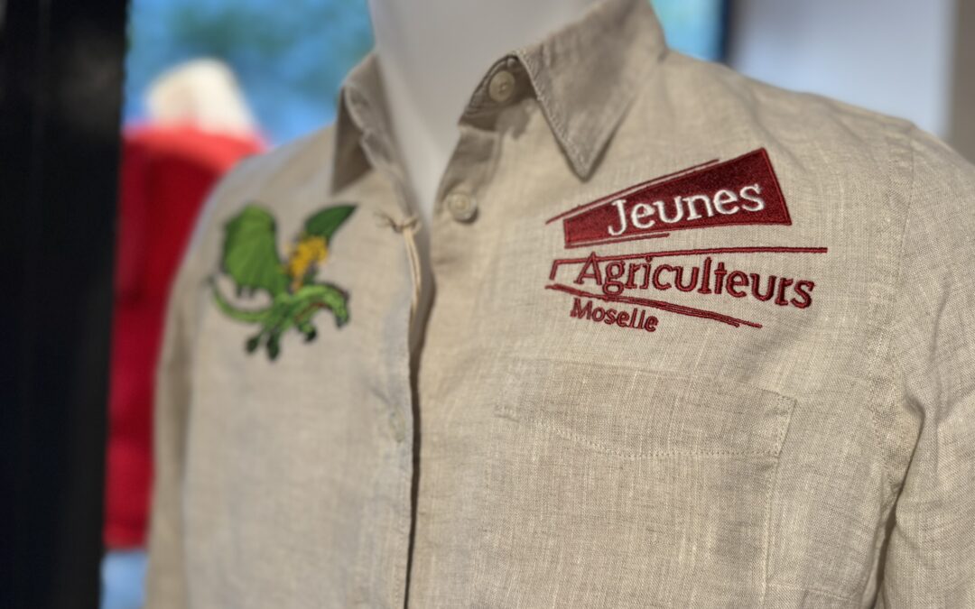 Chemise beige en lin portée sur un mannequin, brodée des inscriptions « Jeunes Agriculteurs Moselle » en rouge, avec un motif végétal vert et jaune sur la poitrine gauche.