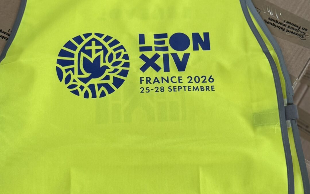 Gilet de sécurité jaune fluorescent « LÉON XIV – FRANCE 2026 – 25-28 SEPTEMBRE », posé sur des cartons.